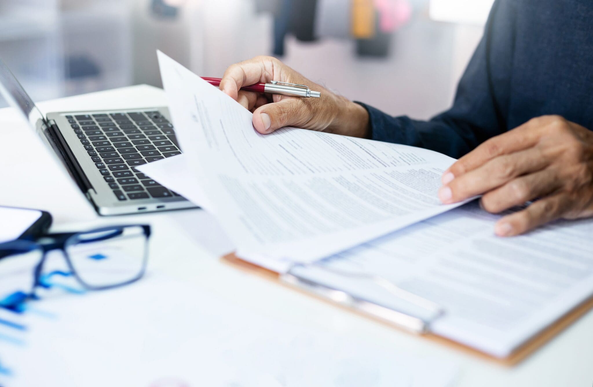 Person reviewing documents with pen and laptop.