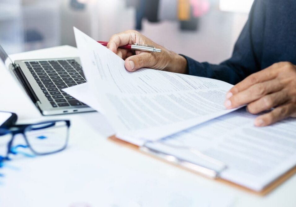 Person reviewing documents with pen and laptop.